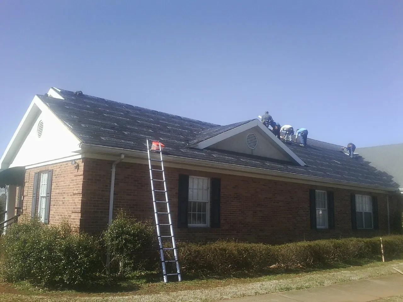 Crew tearing shingles off a brick ranch roof with a ladder set — Emergency Roof Repair work by our crew in Amsterdam
