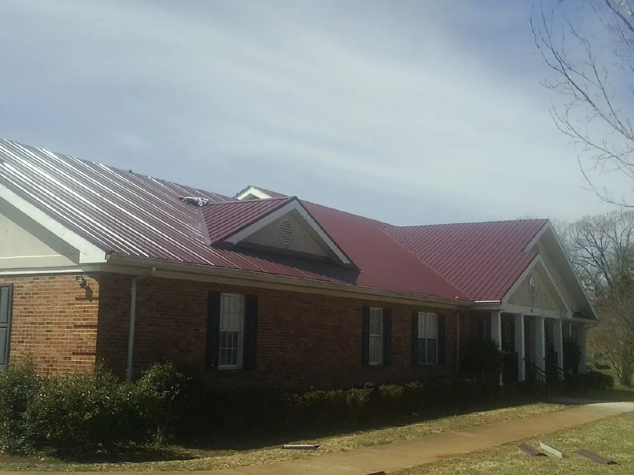 Red metal roof with gabled entries on a long brick building, from a Hail Damage Roof Repair job in Amsterdam
