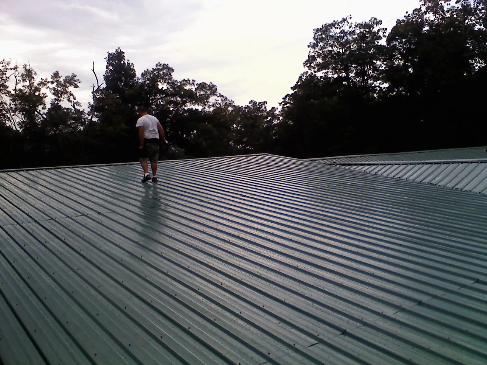 Roofer walking a wide expanse of new green metal roofing in Amsterdam